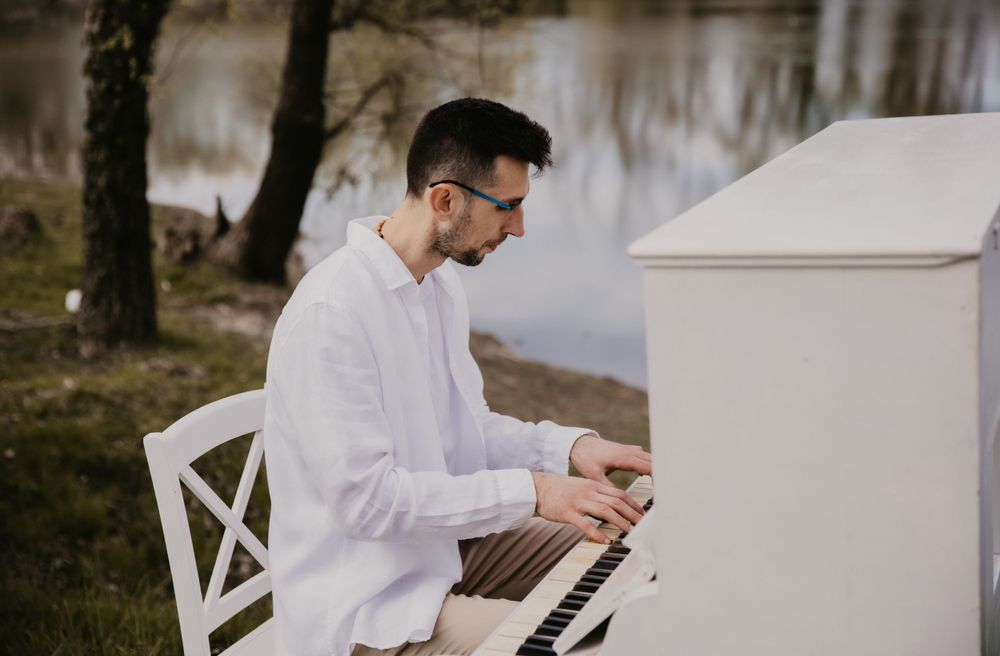 A white piano outdoors near a lake with bare trees in background.