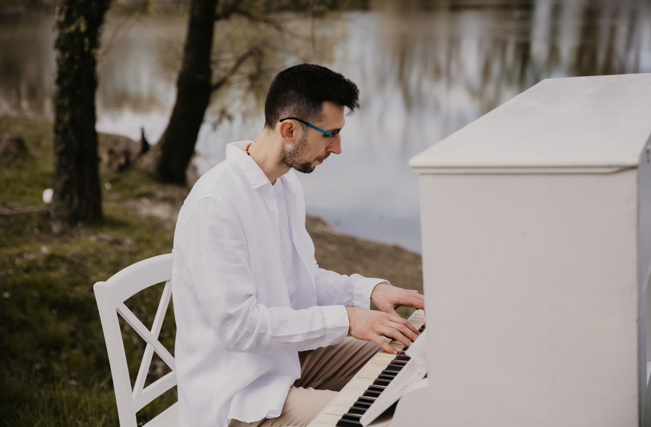 A white piano outdoors near a lake with bare trees in background.