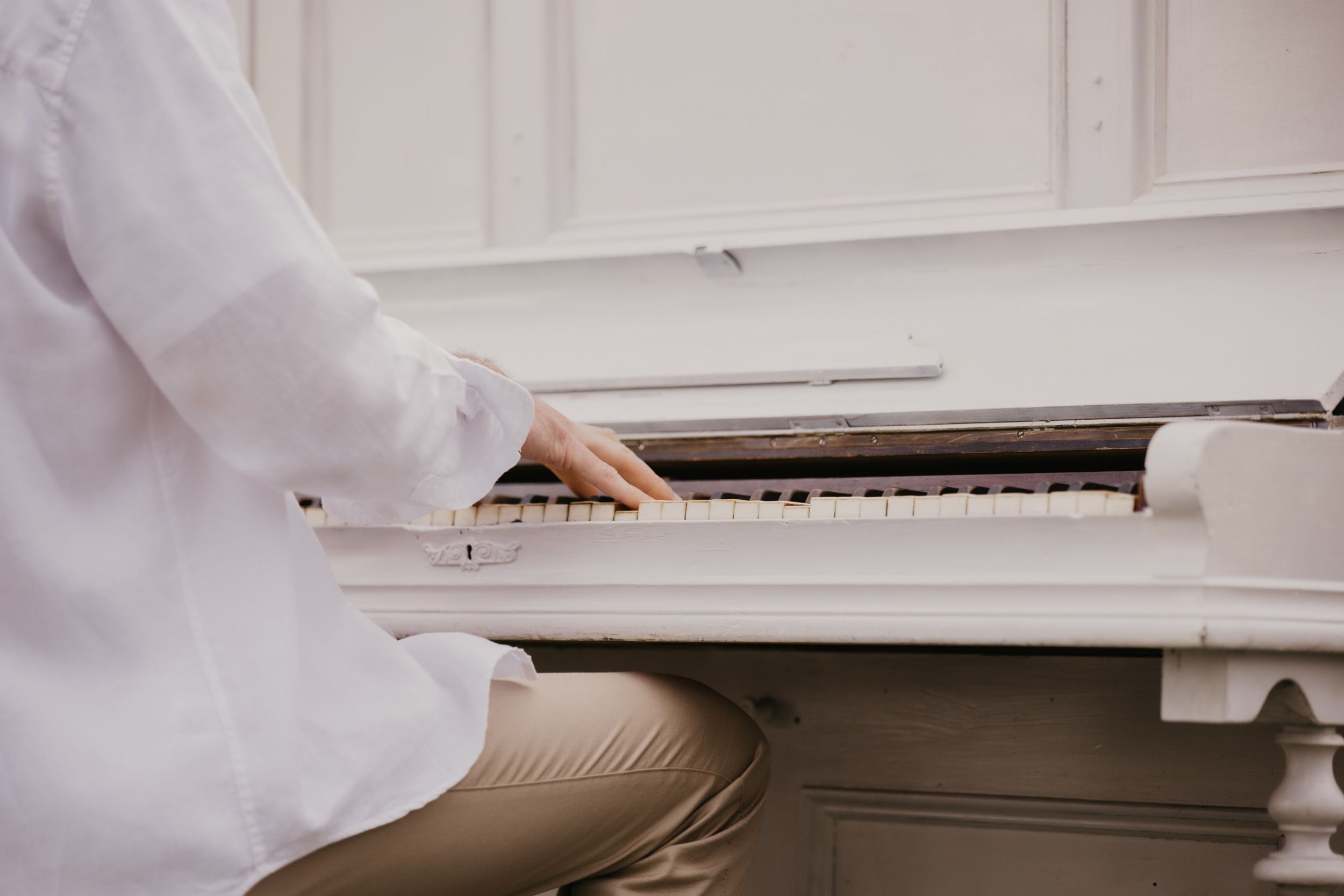 Close-up detail of hands on white piano keys with white sleeve visible.