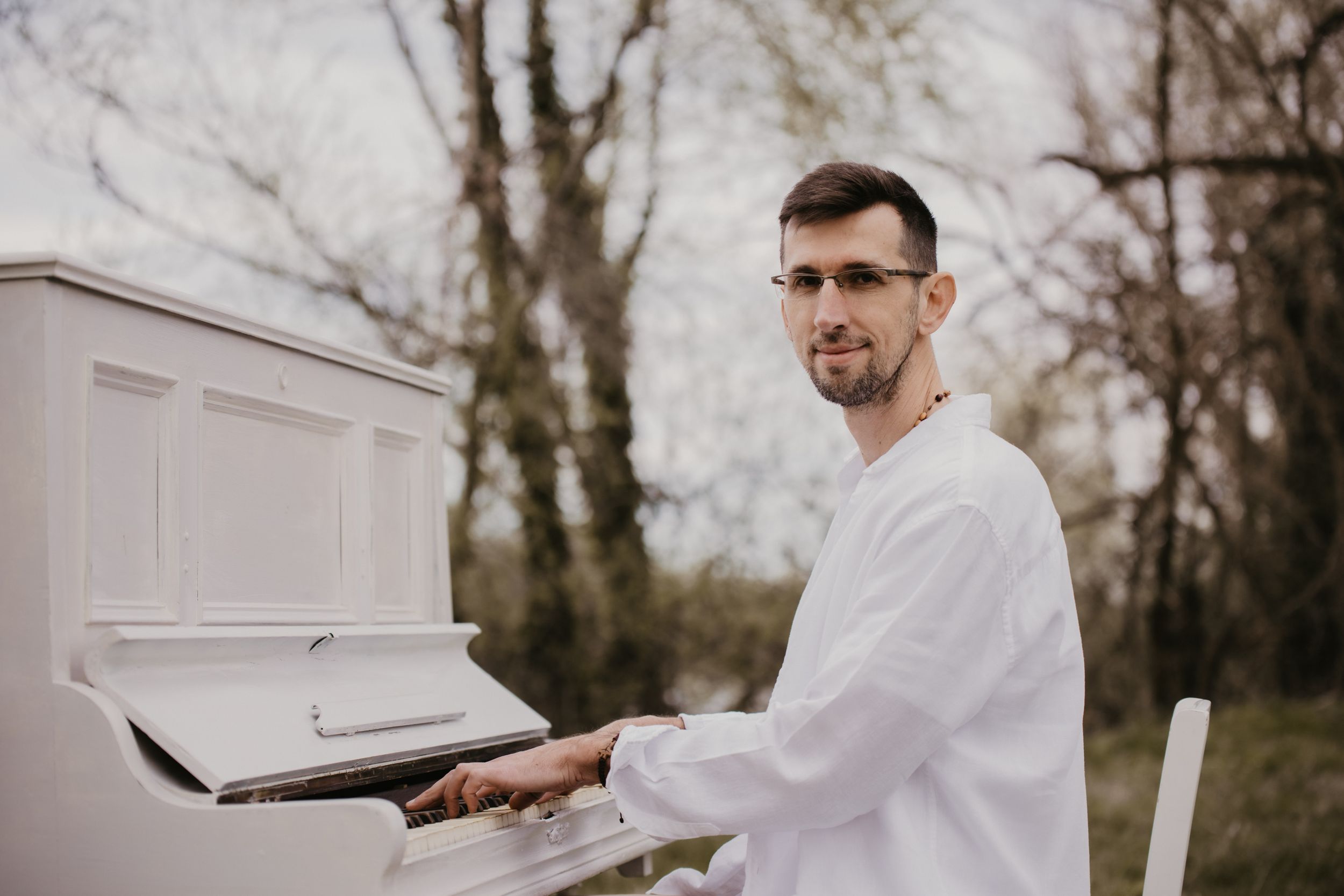 White piano placed outdoors against bare winter trees.