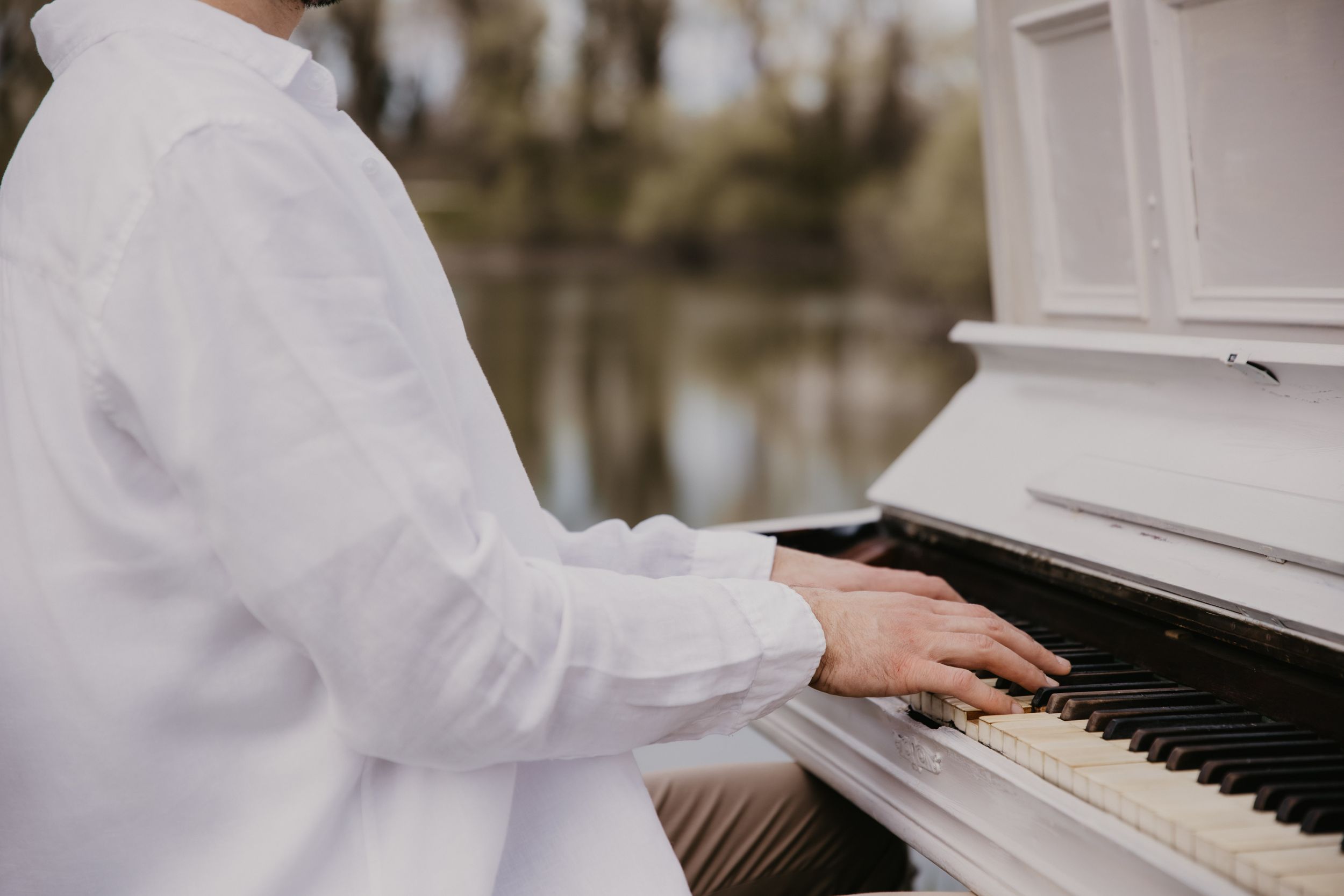 Close-up shot of hands playing white piano keys outdoors.