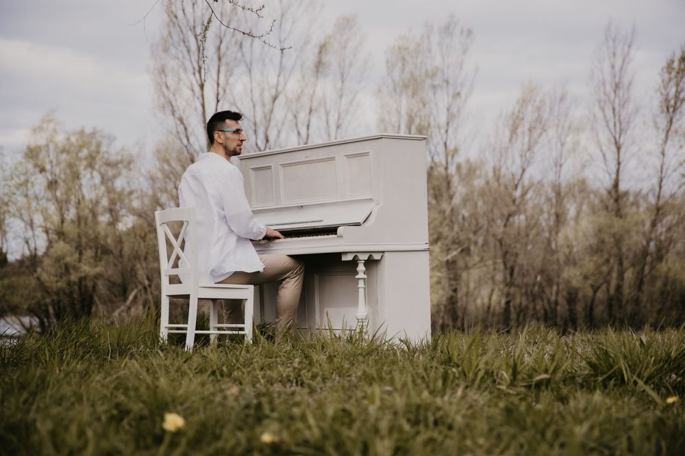 White upright piano placed in grassy field with bare trees in background.