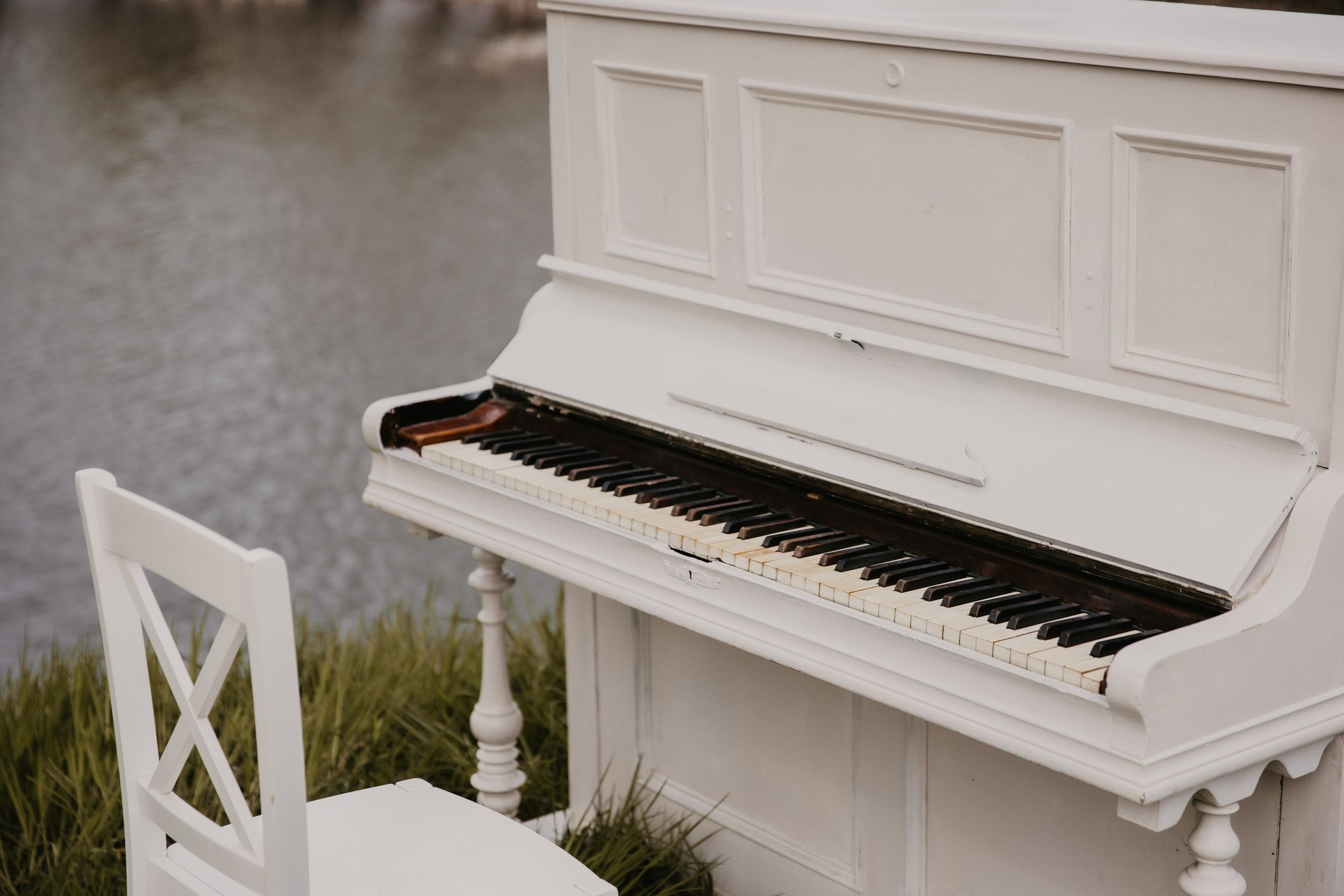 Close-up view of white upright piano placed outdoors near water.