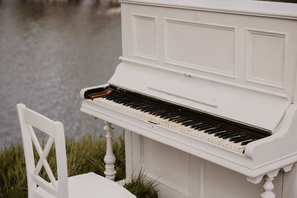 Close-up view of white upright piano placed outdoors near water.