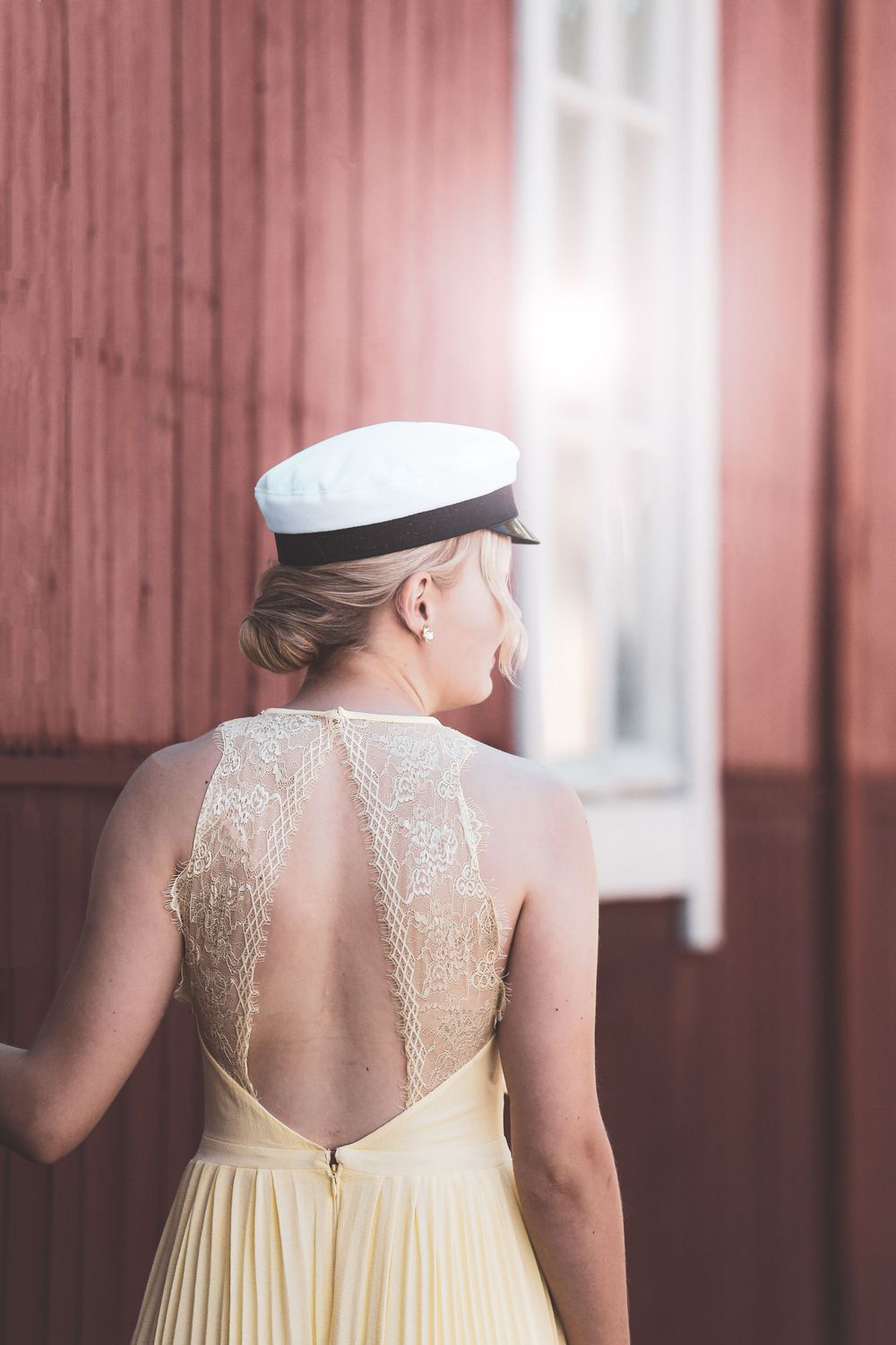 Back view of elegant cream lace dress with sheer illusion detail against red wall.