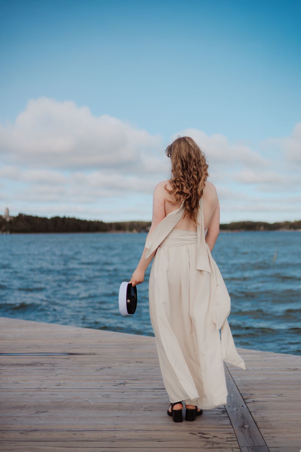 White dress flowing in the breeze on a wooden dock overlooking blue waters.
