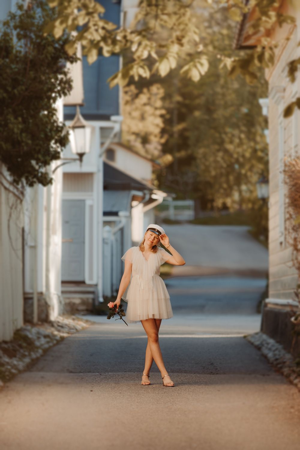 Person in light dress twirling on a sunlit path between white buildings.