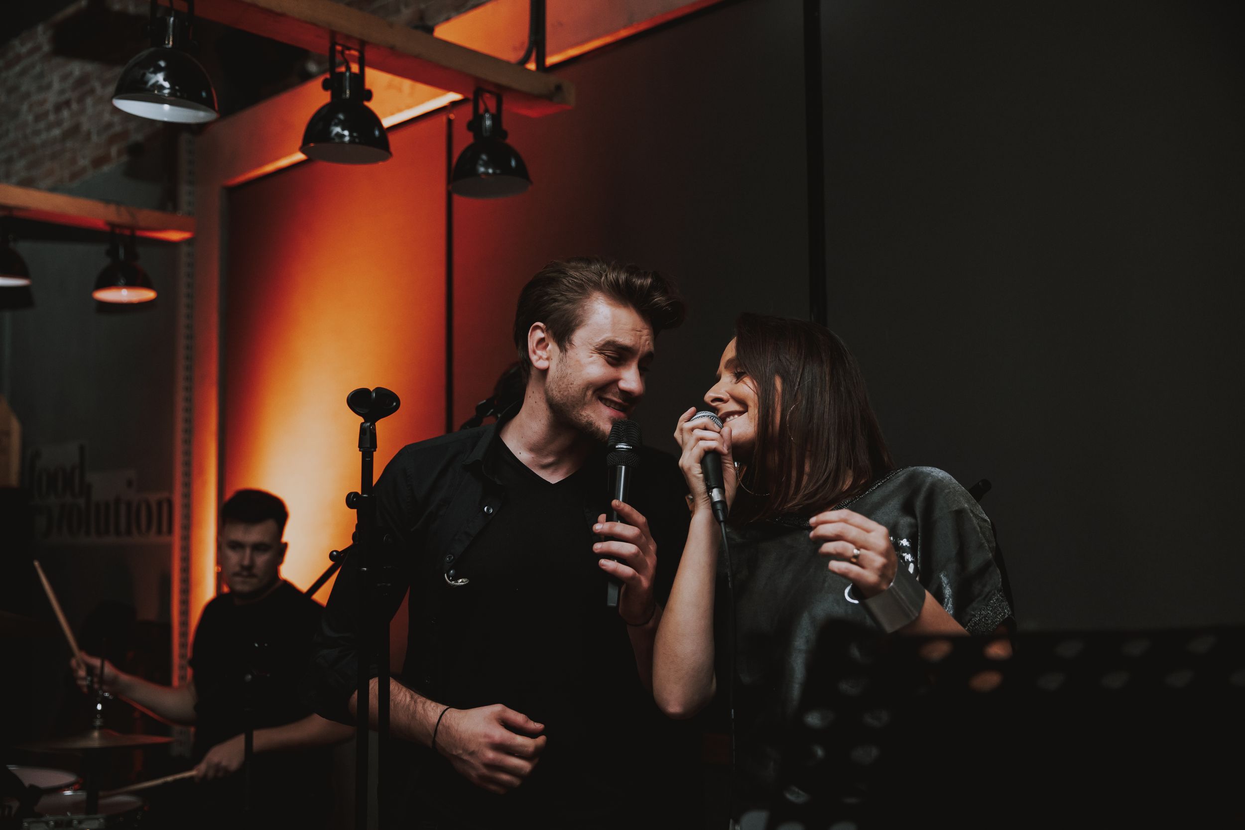 Two people sharing a laugh while holding microphones in a dimly lit venue.