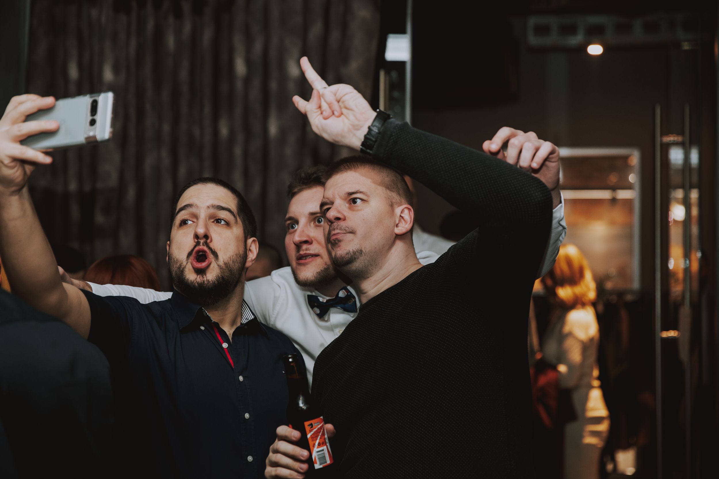 Friends taking selfies and making gestures at a bar.