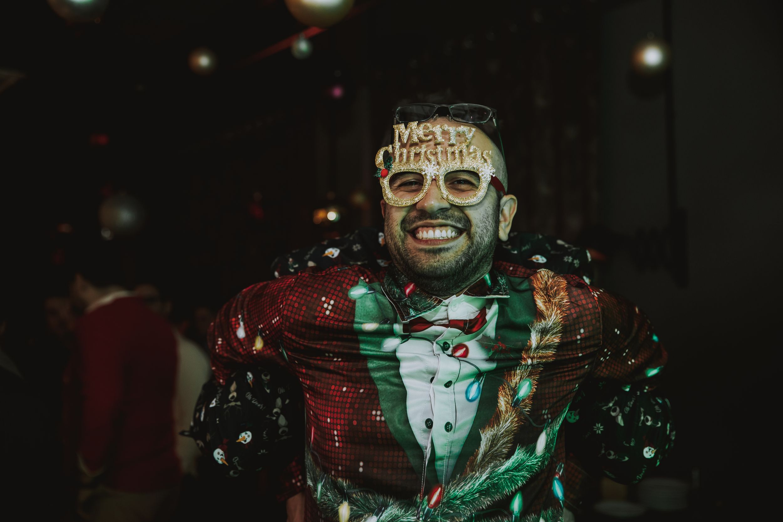 Person wearing festive face paint and costume smiling under colorful party lights.