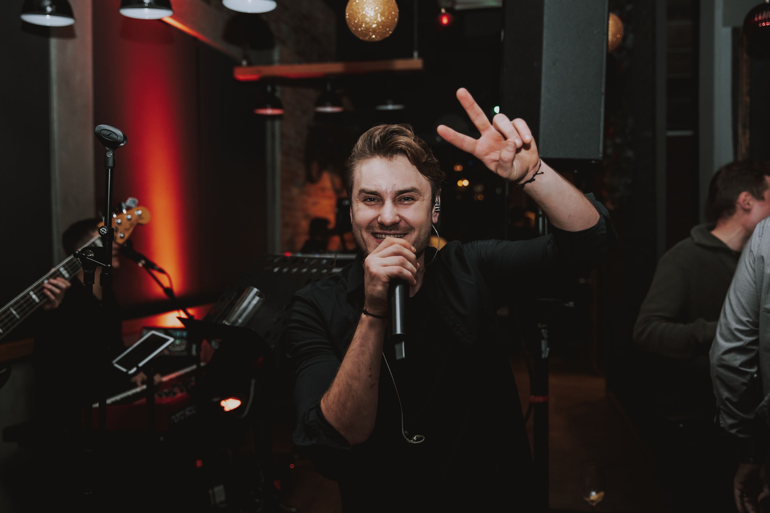 Person making peace sign while holding microphone in dark venue with red lighting.