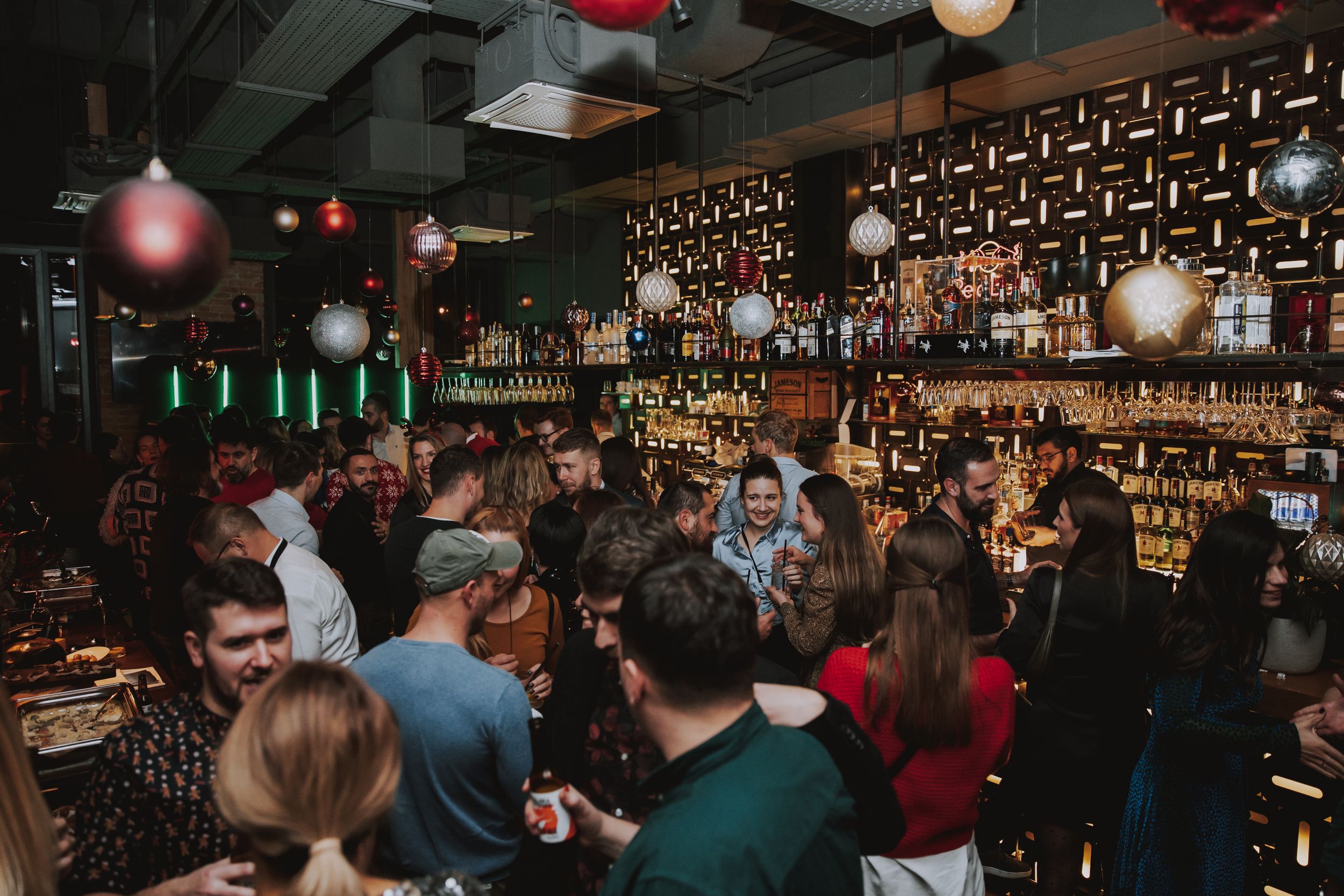 A crowded bar scene with patrons gathering around the counter under ambient lighting.