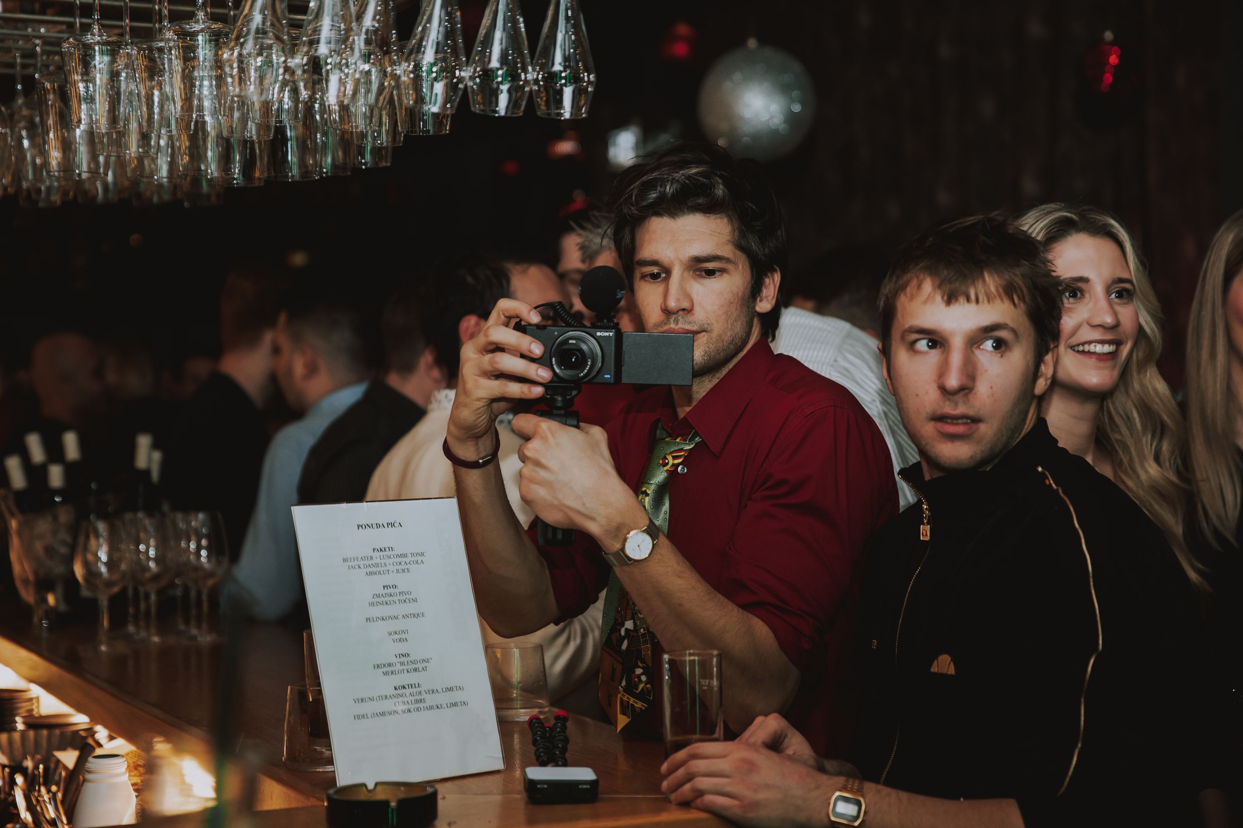 Group of patrons at a bar counter examining a menu in low light.