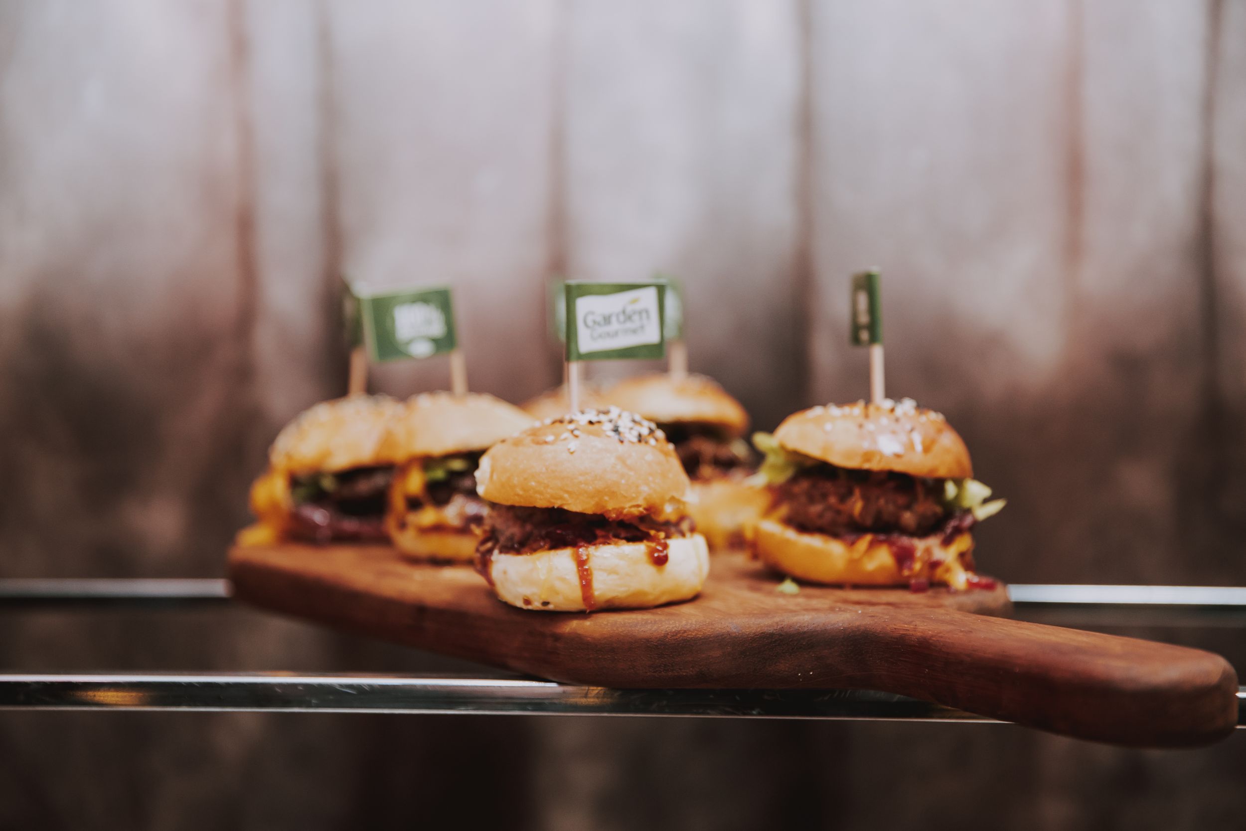 Appetizing slider burgers on a wooden serving board with small flag picks.
