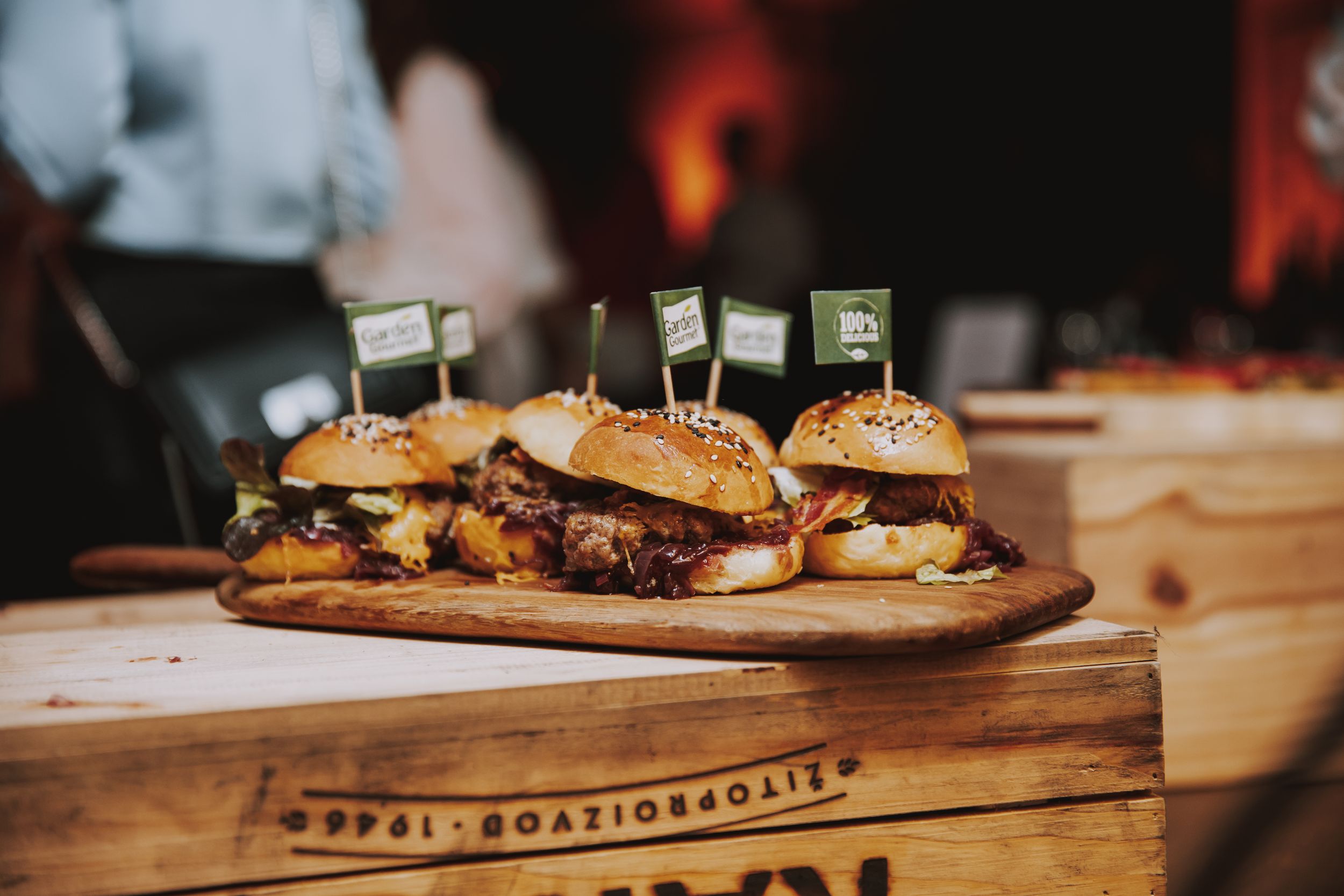Gourmet mini burgers served on a wooden board with decorative picks.