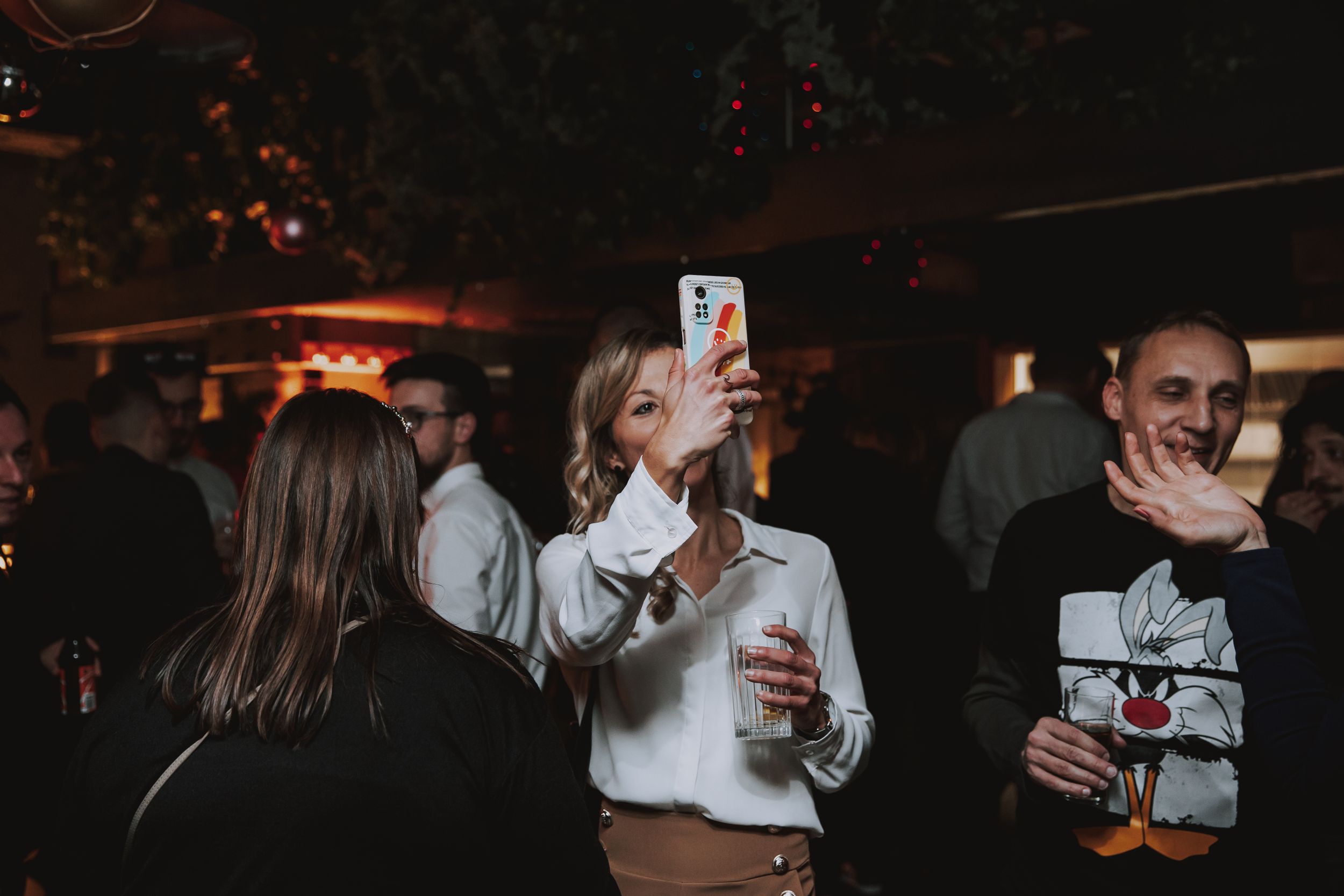 People taking selfies and enjoying drinks at a dimly lit bar.