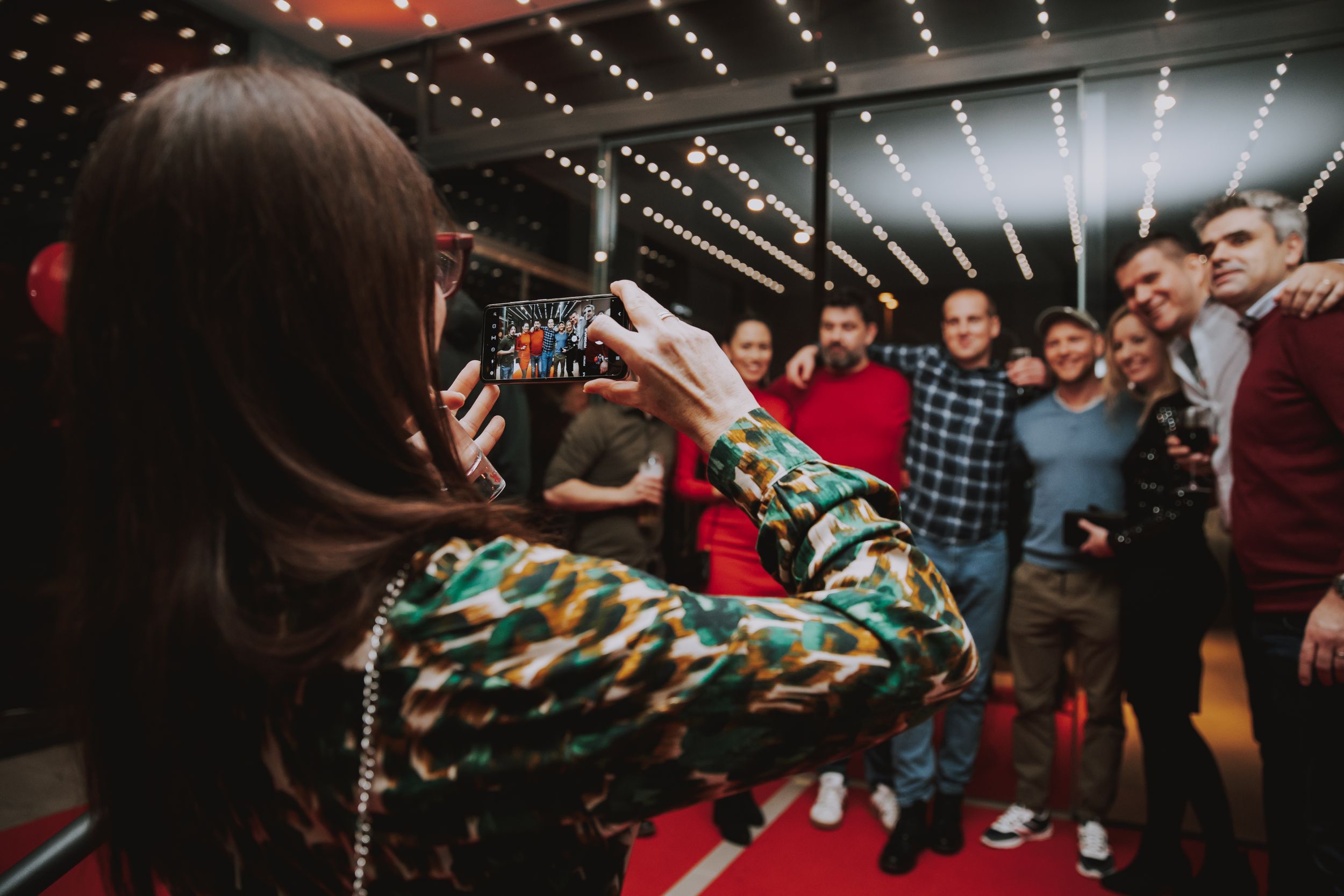 Someone taking a photo of a group at a party with string lights in the background.