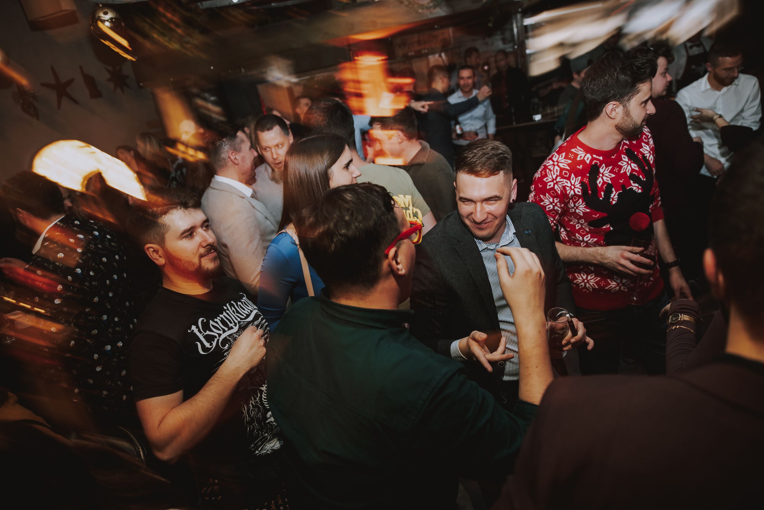 Crowded nightclub scene with people dancing and socializing under dim lighting.