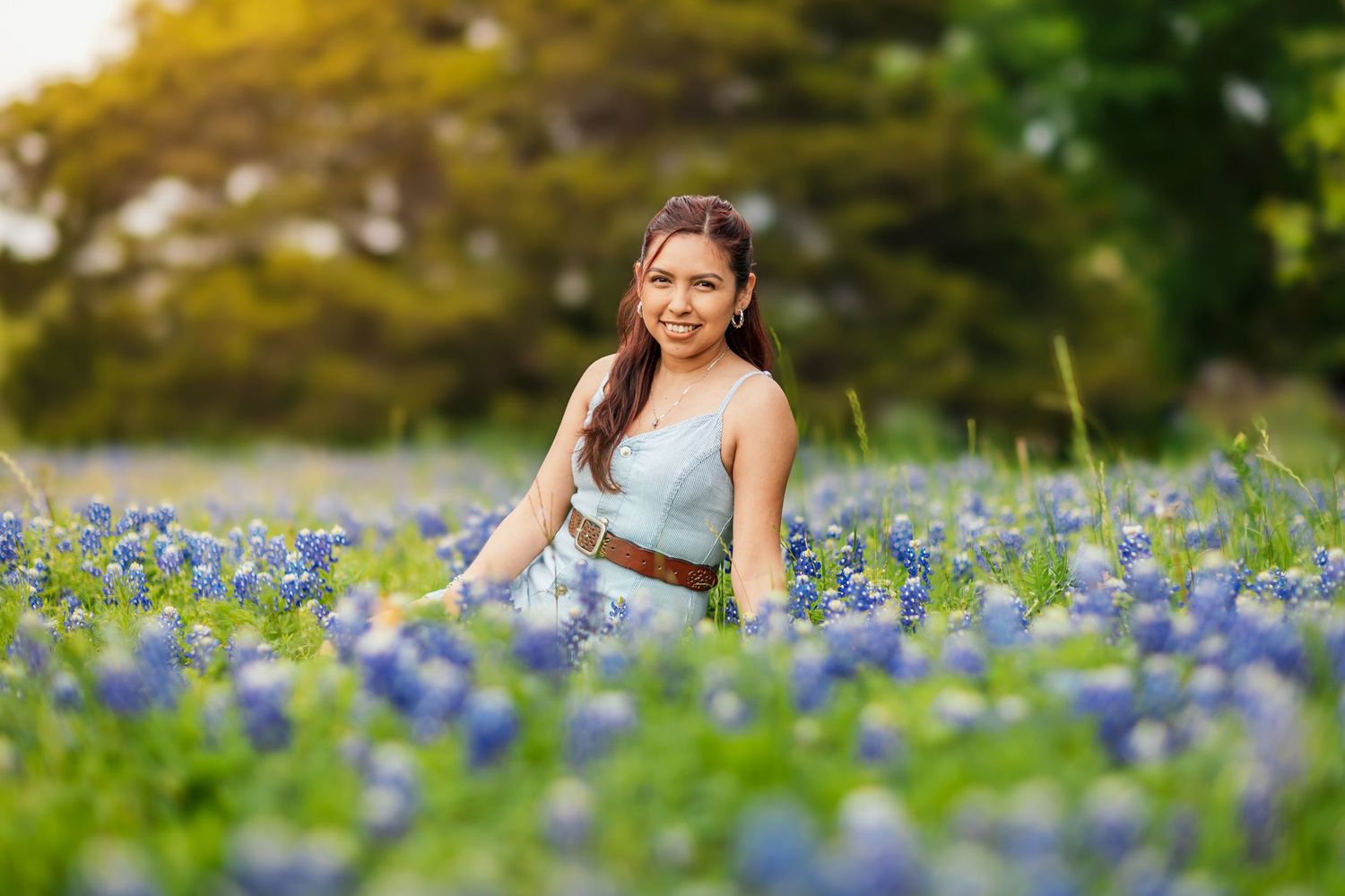 A person sits in a field of blooming blue Texas bluebonnets during golden hour.