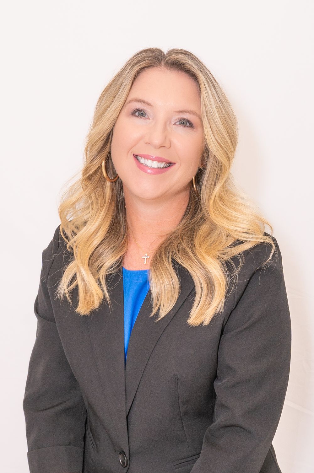 Professional headshot of person in dark blazer and blue top against white background.