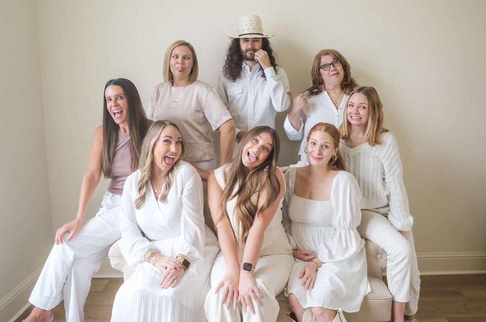 Group portrait of people wearing white outfits sitting together in casual indoor setting.