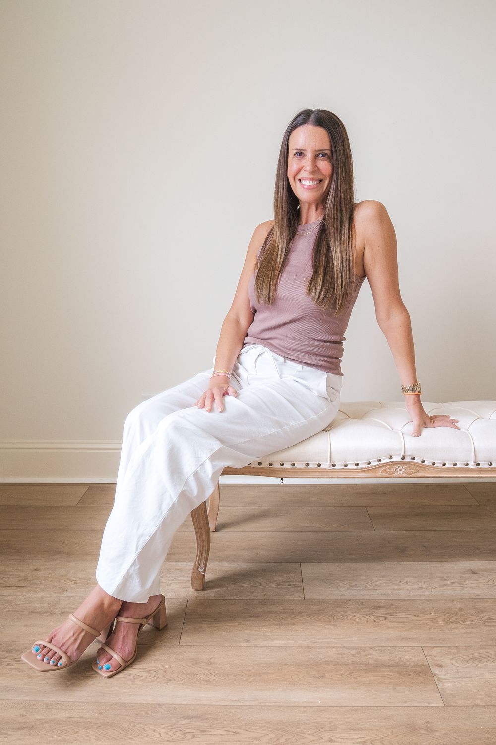 Casual portrait of person in pink top and white pants sitting on bench.