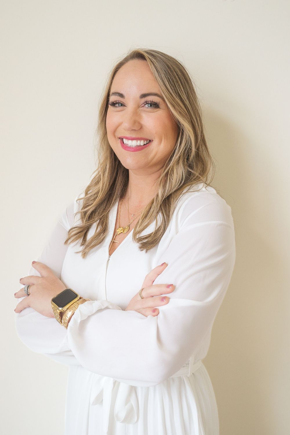 Professional portrait of person in white blazer with gold watch and crossed arms.