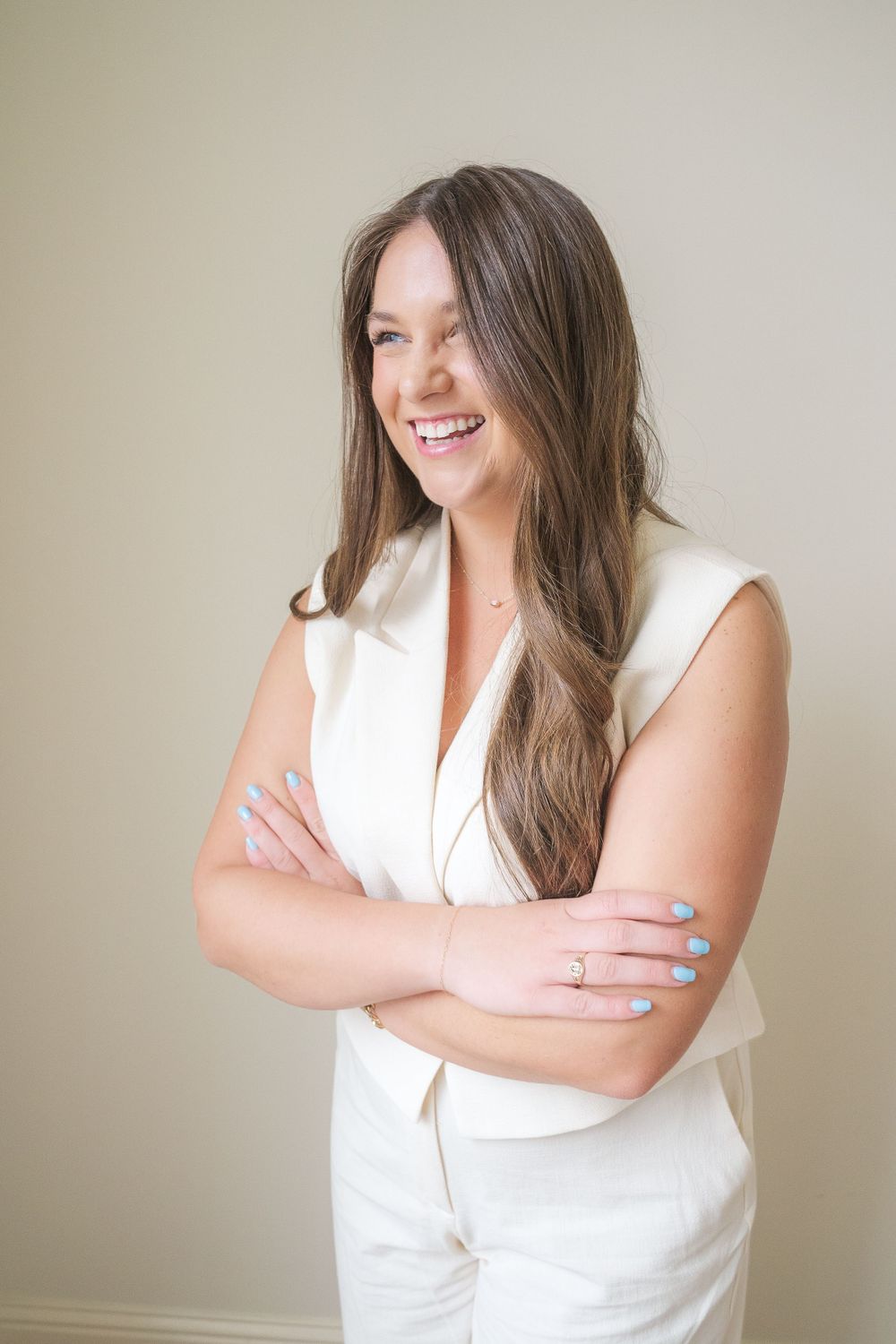 Business portrait of person in white outfit smiling with crossed arms.