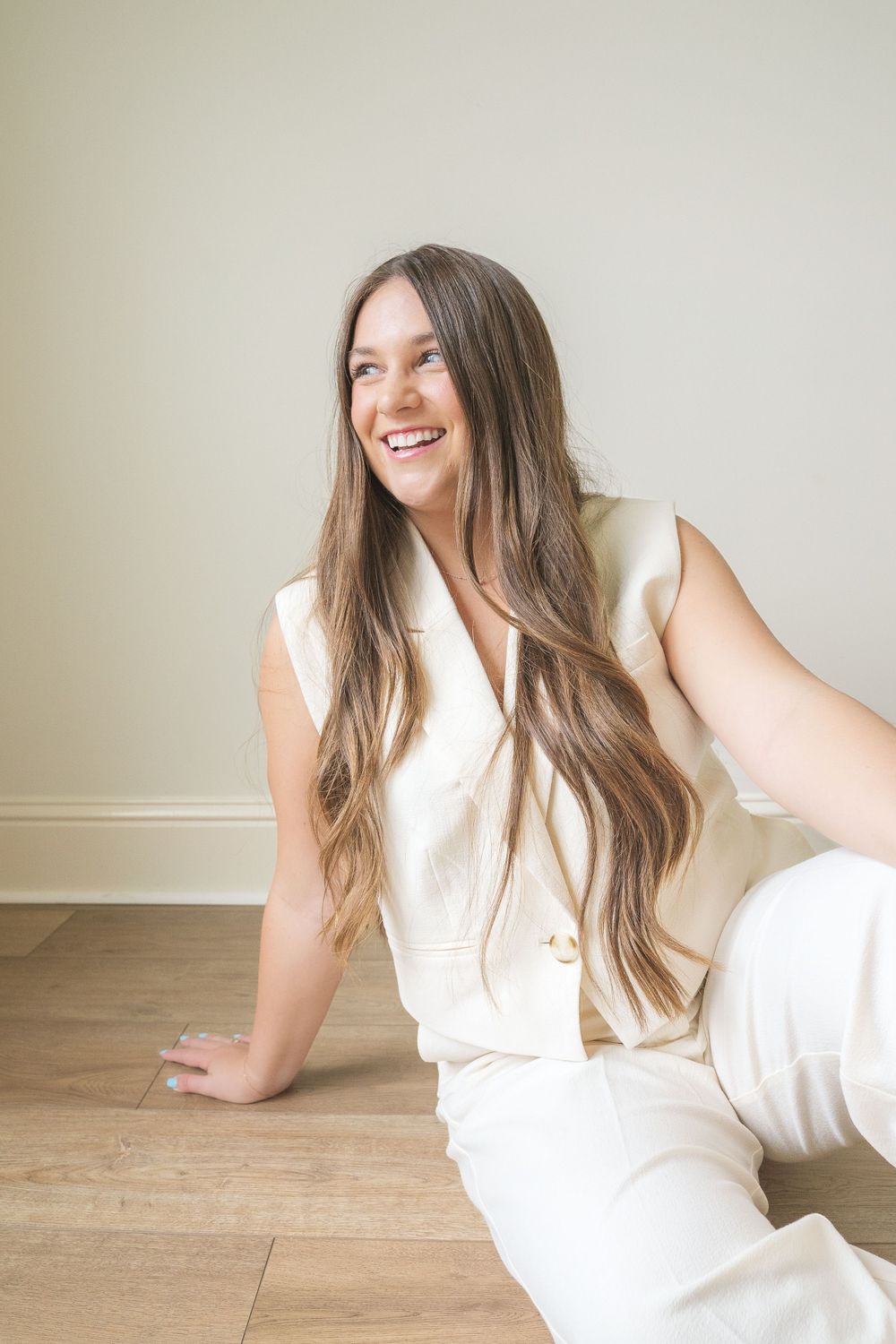 Casual portrait of person in white outfit sitting on wooden floor.