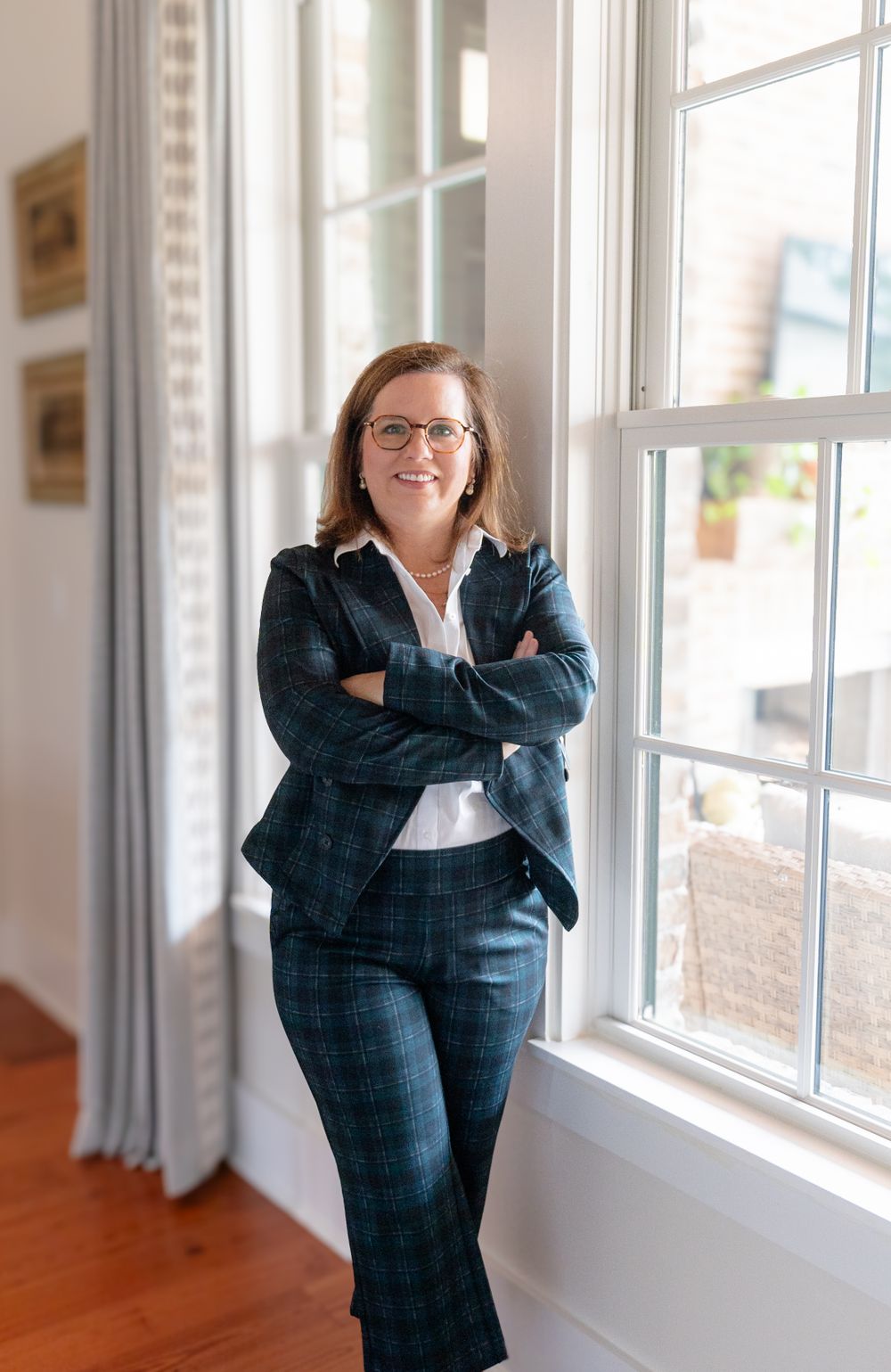Professional portrait of person wearing plaid suit standing by bright window.