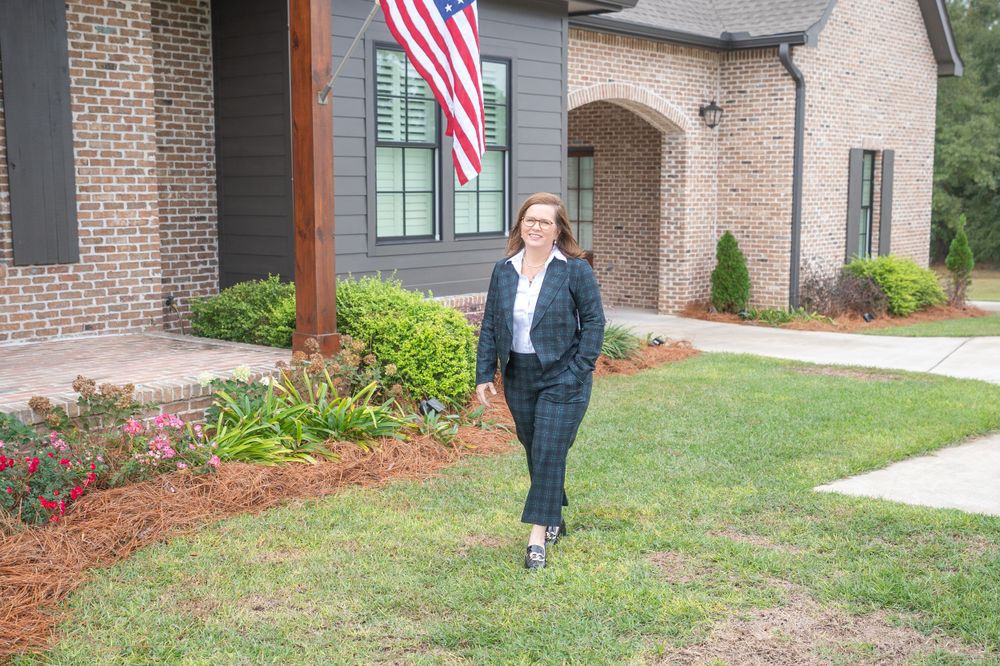 Person in business attire walking outside brick house with American flag.