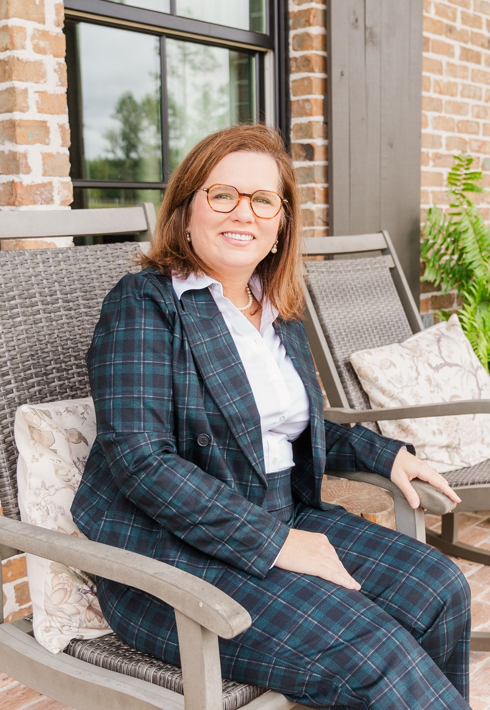 Professional portrait of person in plaid blazer sitting on outdoor patio furniture.