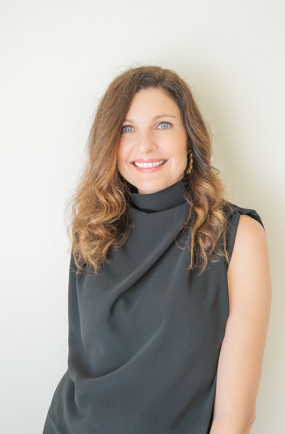 Portrait of person wearing black turtleneck against white wall.