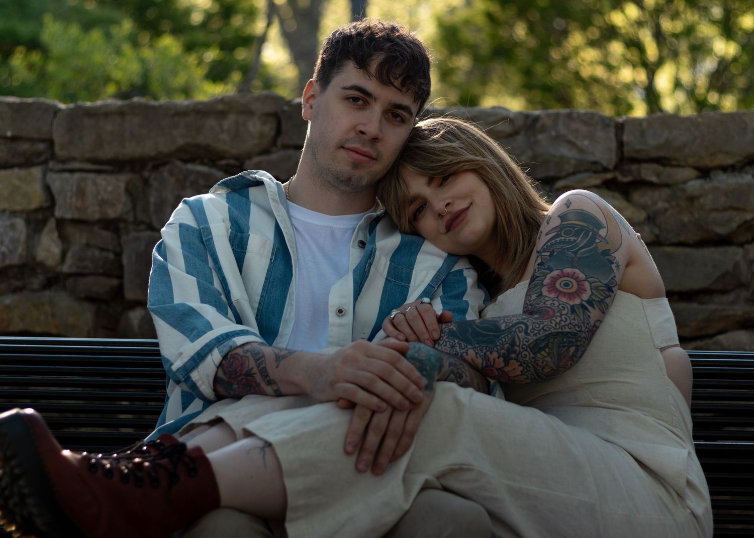 Tattooed couple cuddling on a bench in the park at sunset