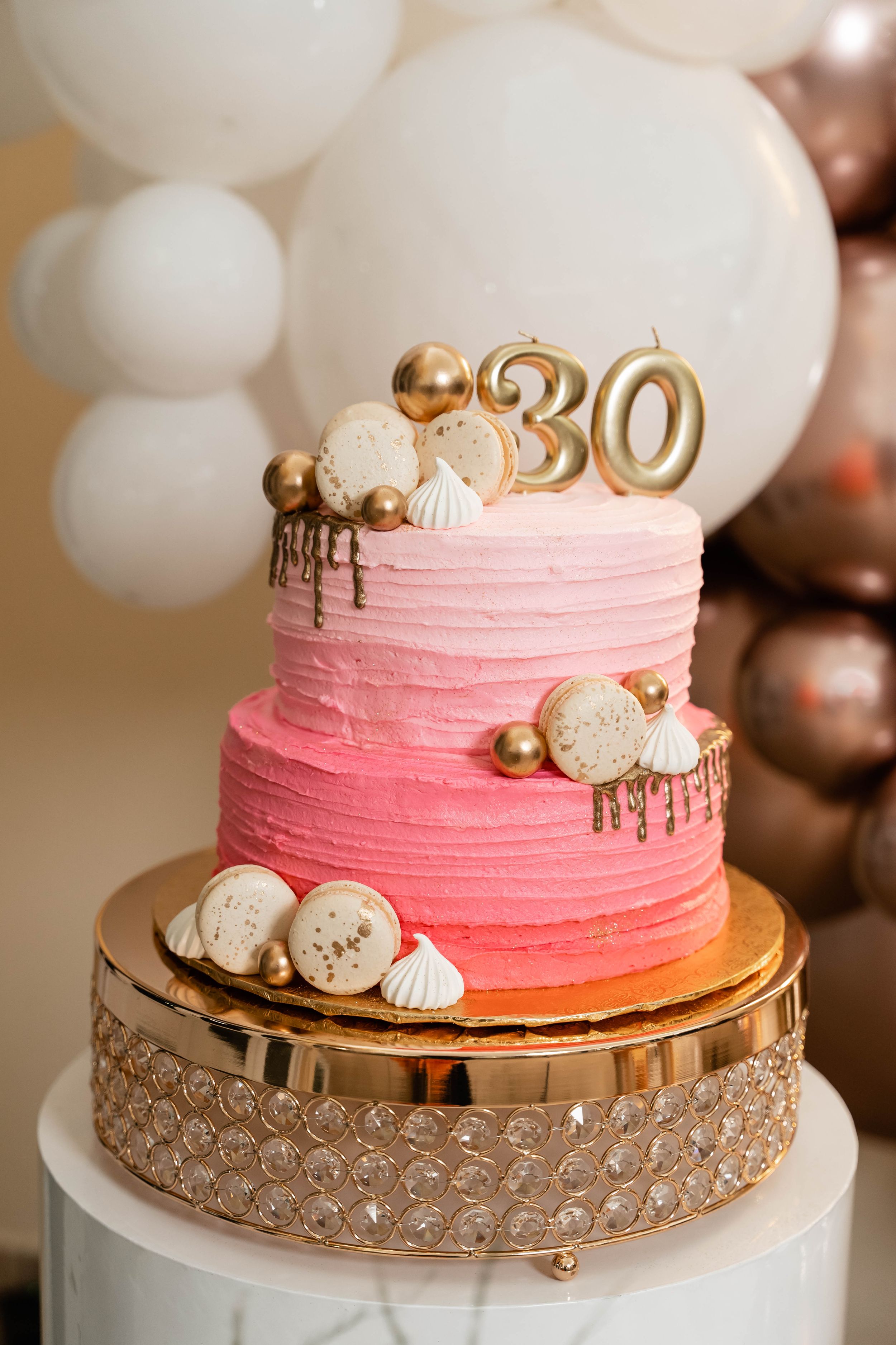 Pink ombre birthday cake with gold 30 topper and white meringues on crystal cake stand.