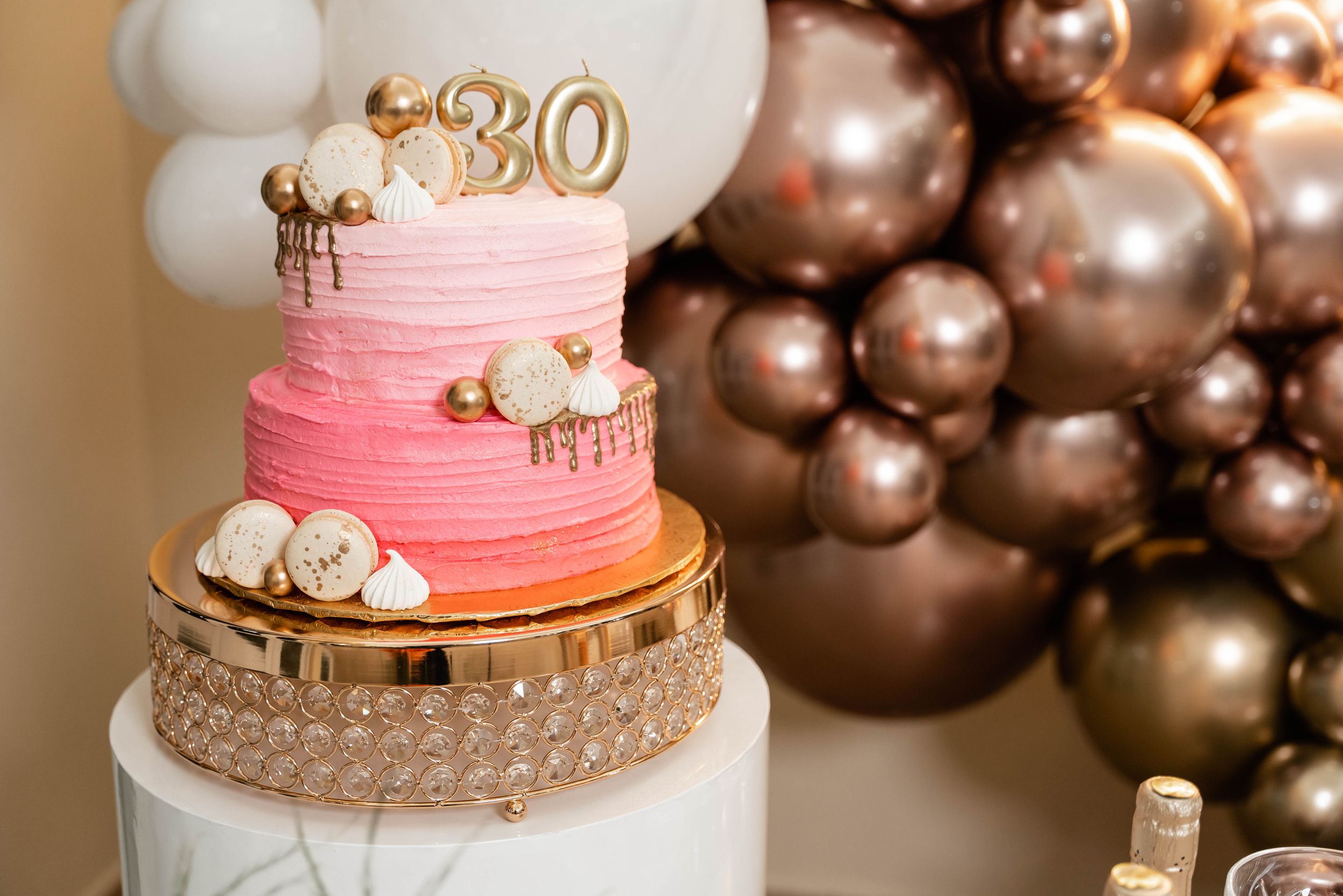 Pink ombre 30th birthday cake with balloon arch and gold accents.