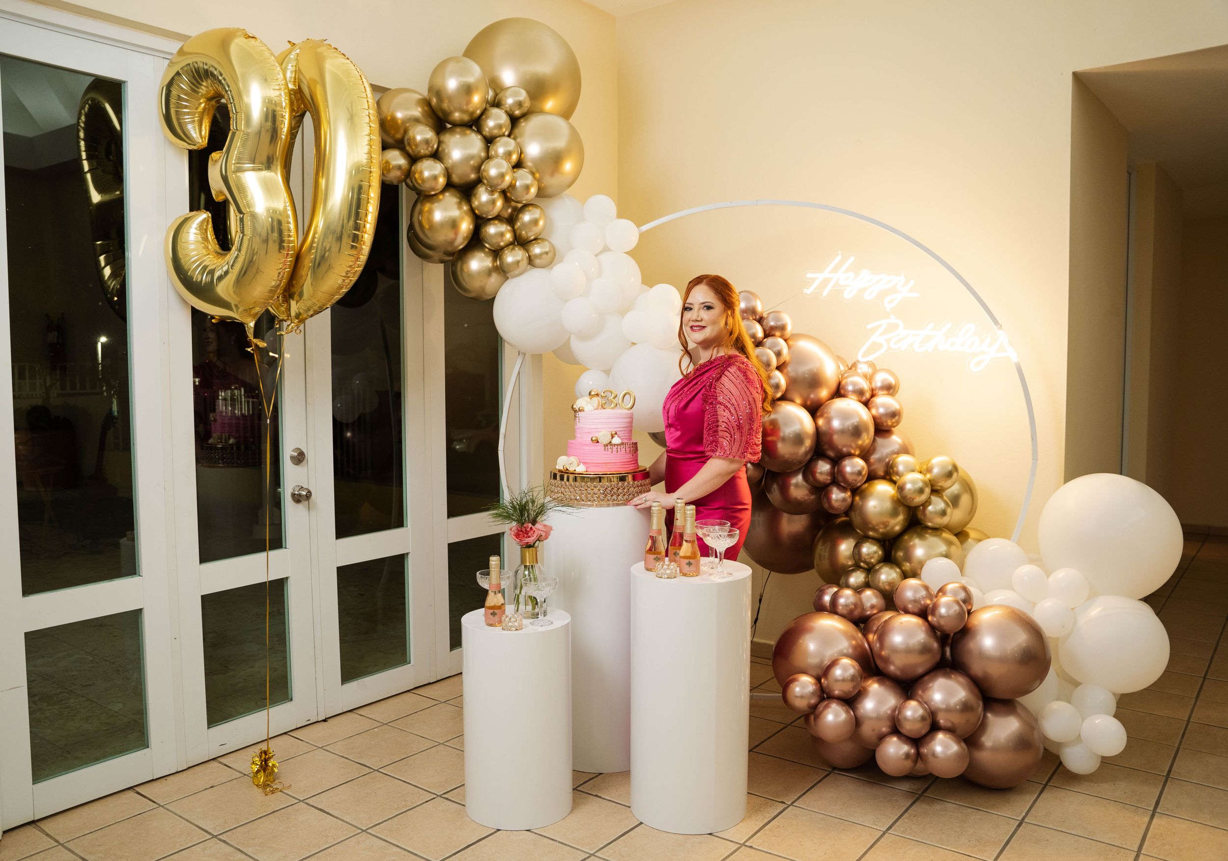 Elegant 30th birthday party setup with gold balloons, white pedestals and rose gold balloon arch decorations.