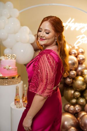 Magenta evening gown against white and gold balloon backdrop with illuminated sign.
