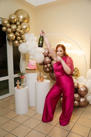 Festive party scene with champagne bottle, pink cake, and elegant balloon decorations.