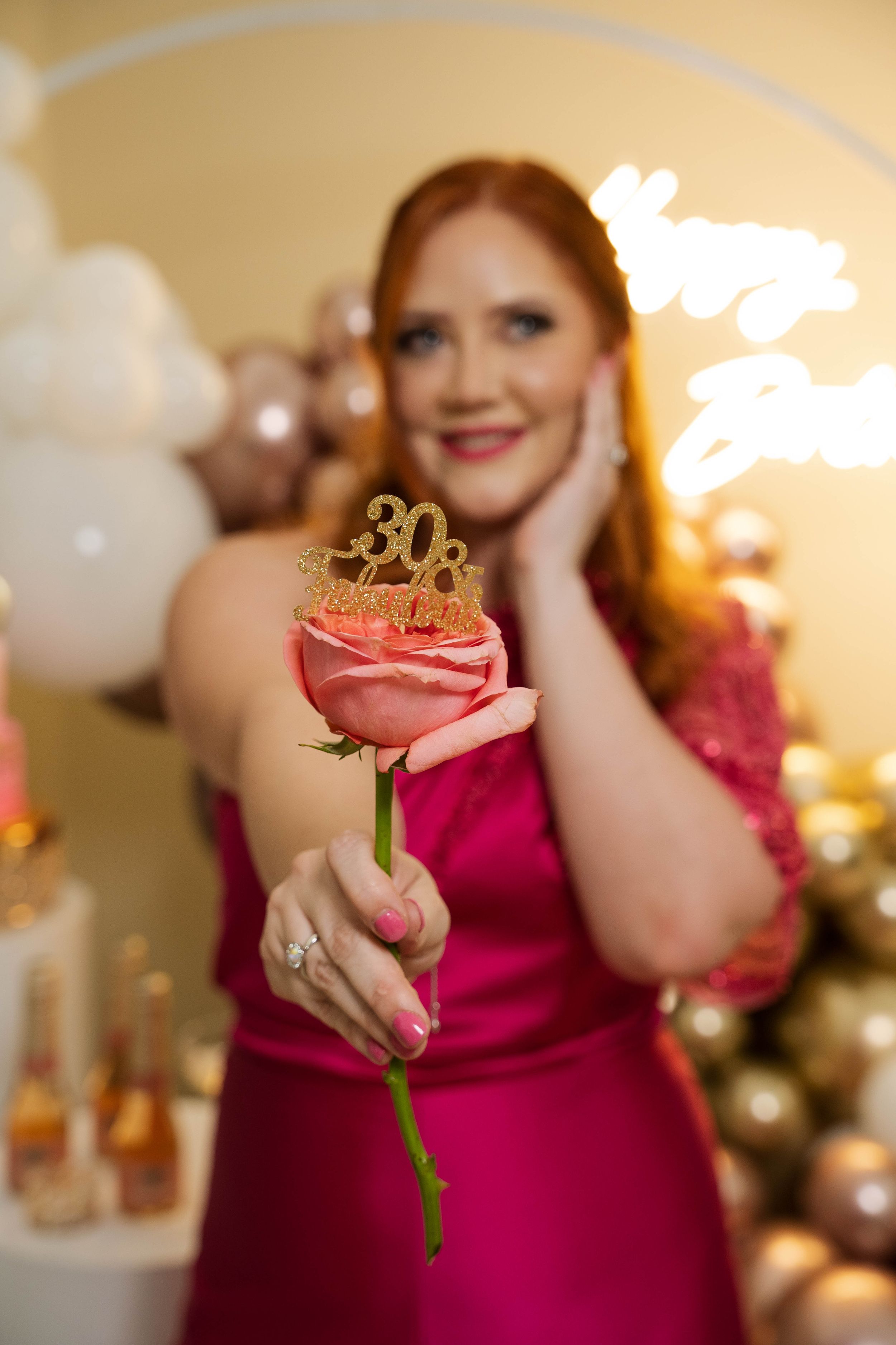 Close-up of pink rose with gold '30' cake topper at elegant birthday celebration.