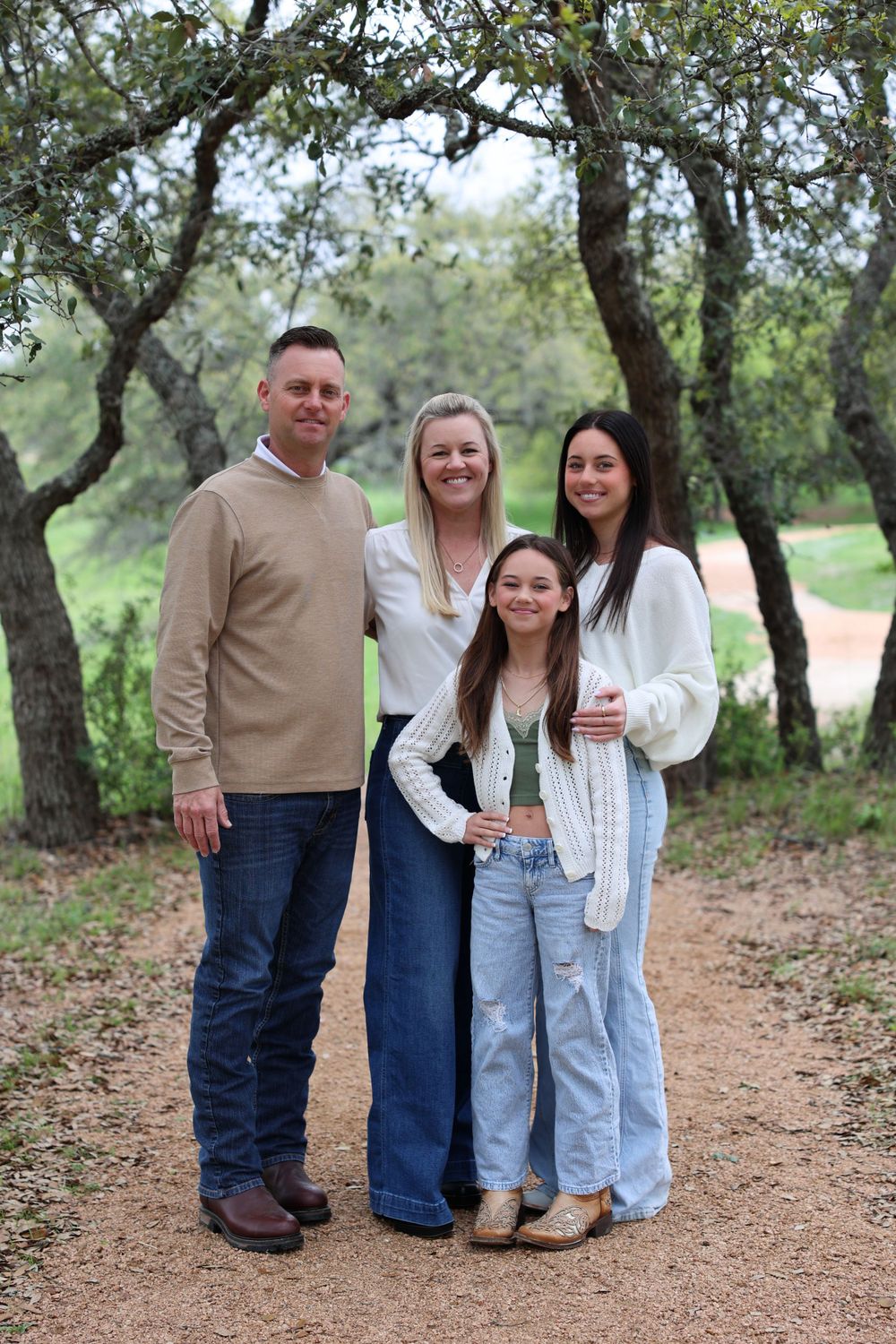 Family group standing together on a dirt path surrounded by oak trees.