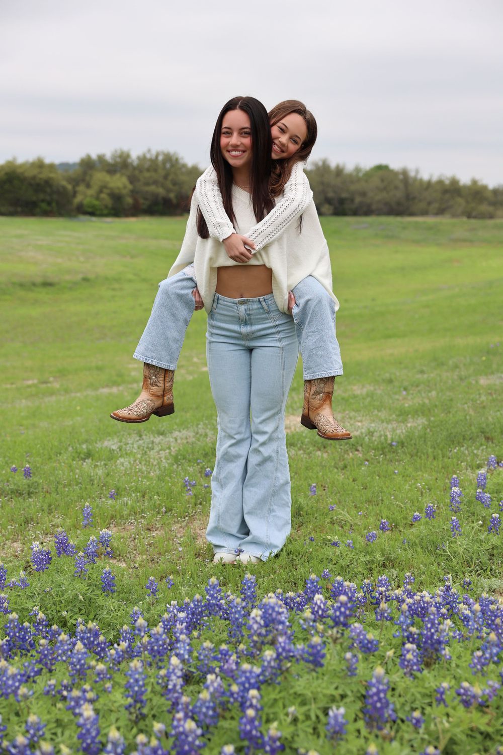 Two people posing playfully in a field of bluebonnets with one getting a piggyback ride.