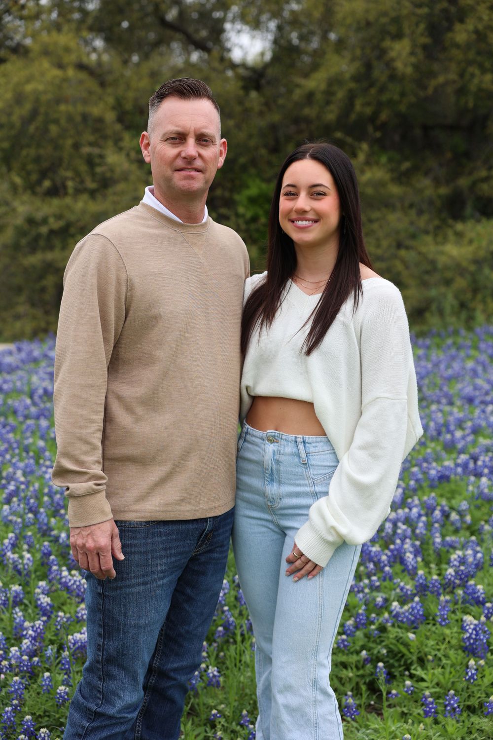 Two people standing together in a field of bluebonnets wearing casual spring attire.