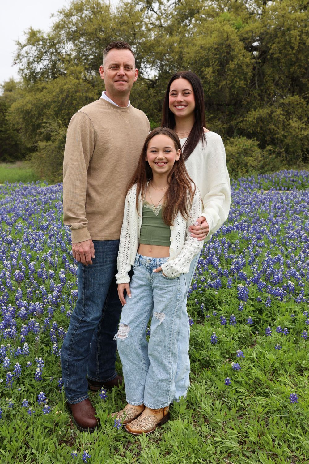 Three people posing together in a blooming bluebonnet field wearing coordinated outfits.