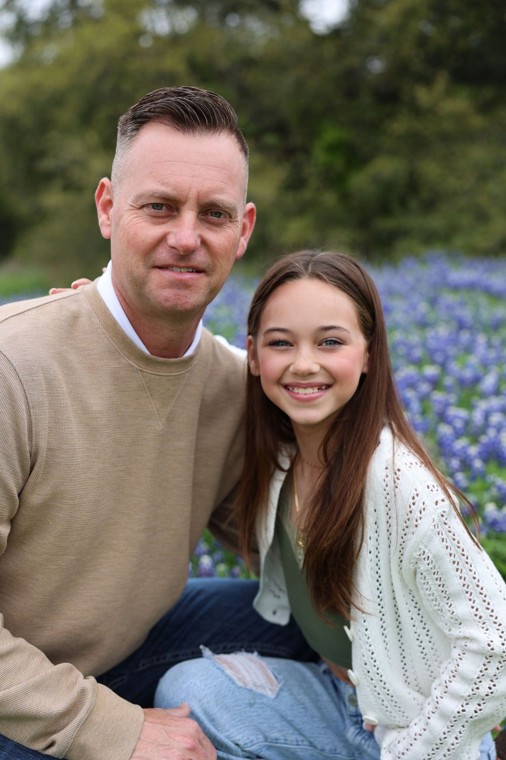 Close-up portrait of two people smiling together in a field of bluebonnets.