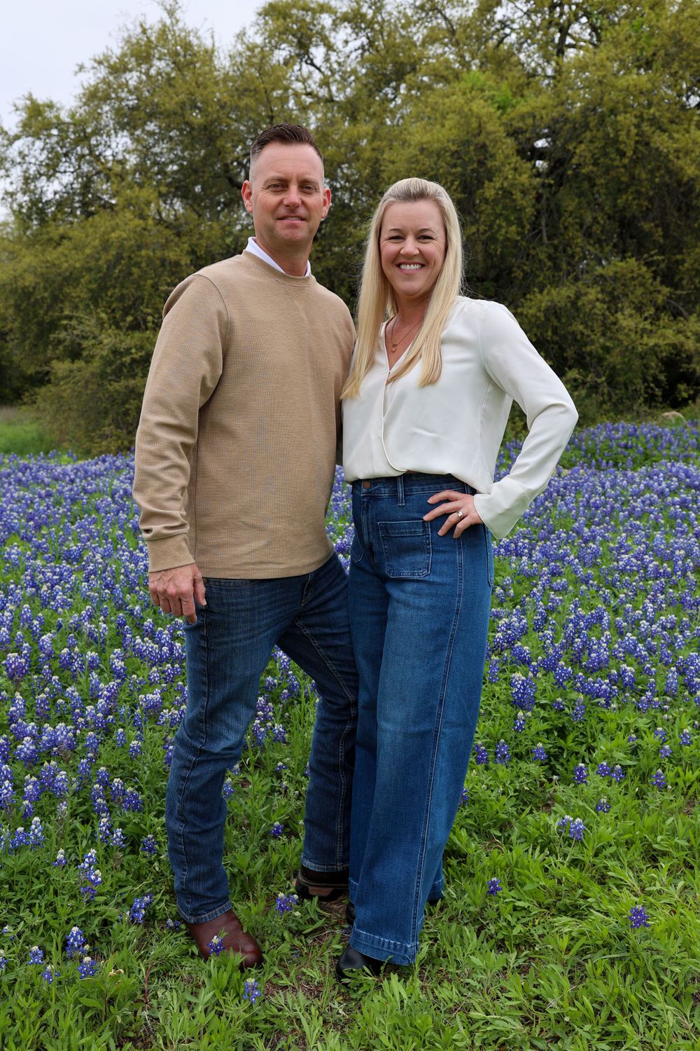 Couple posing together in a field of bluebonnets wearing casual spring clothing.