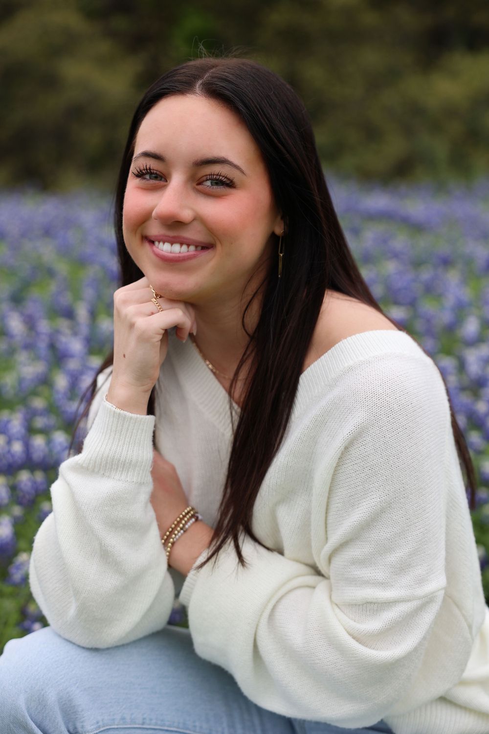 Portrait in a bluebonnet field wearing a white sweater and resting chin on hand.