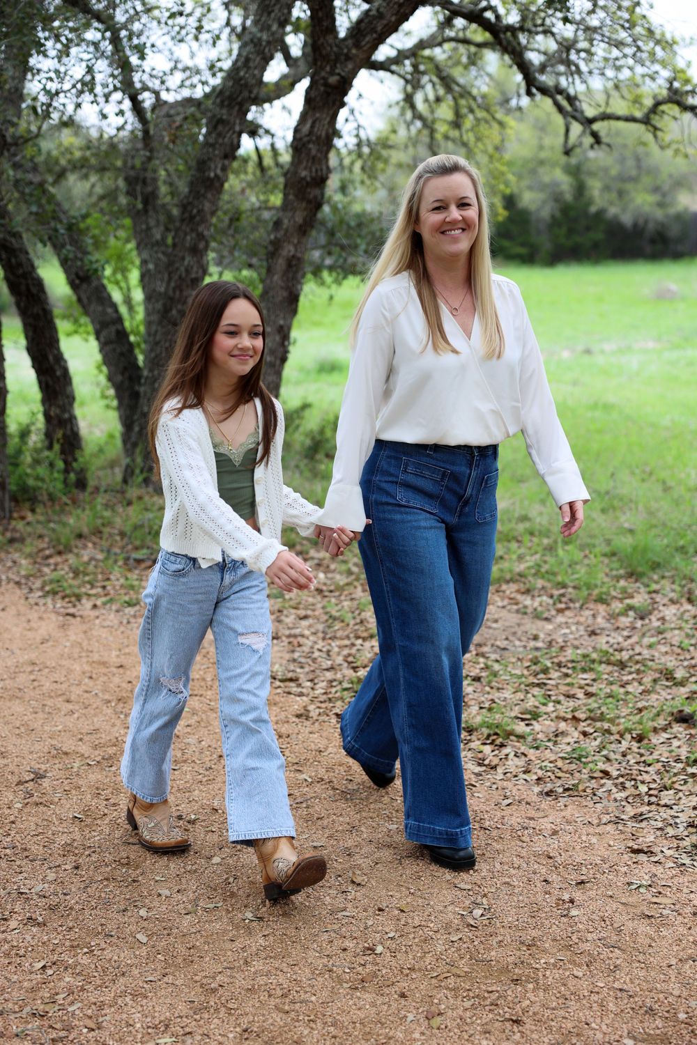 Two people walking hand in hand along a scenic dirt trail surrounded by trees.