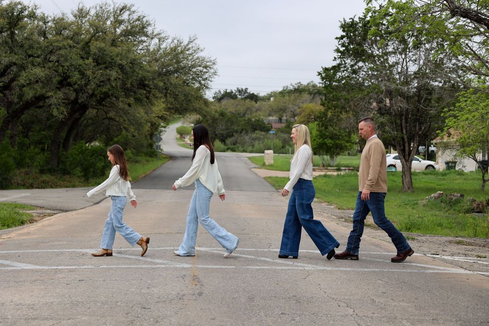 Group walking across a road in matching denim and white outfits against a natural backdrop.