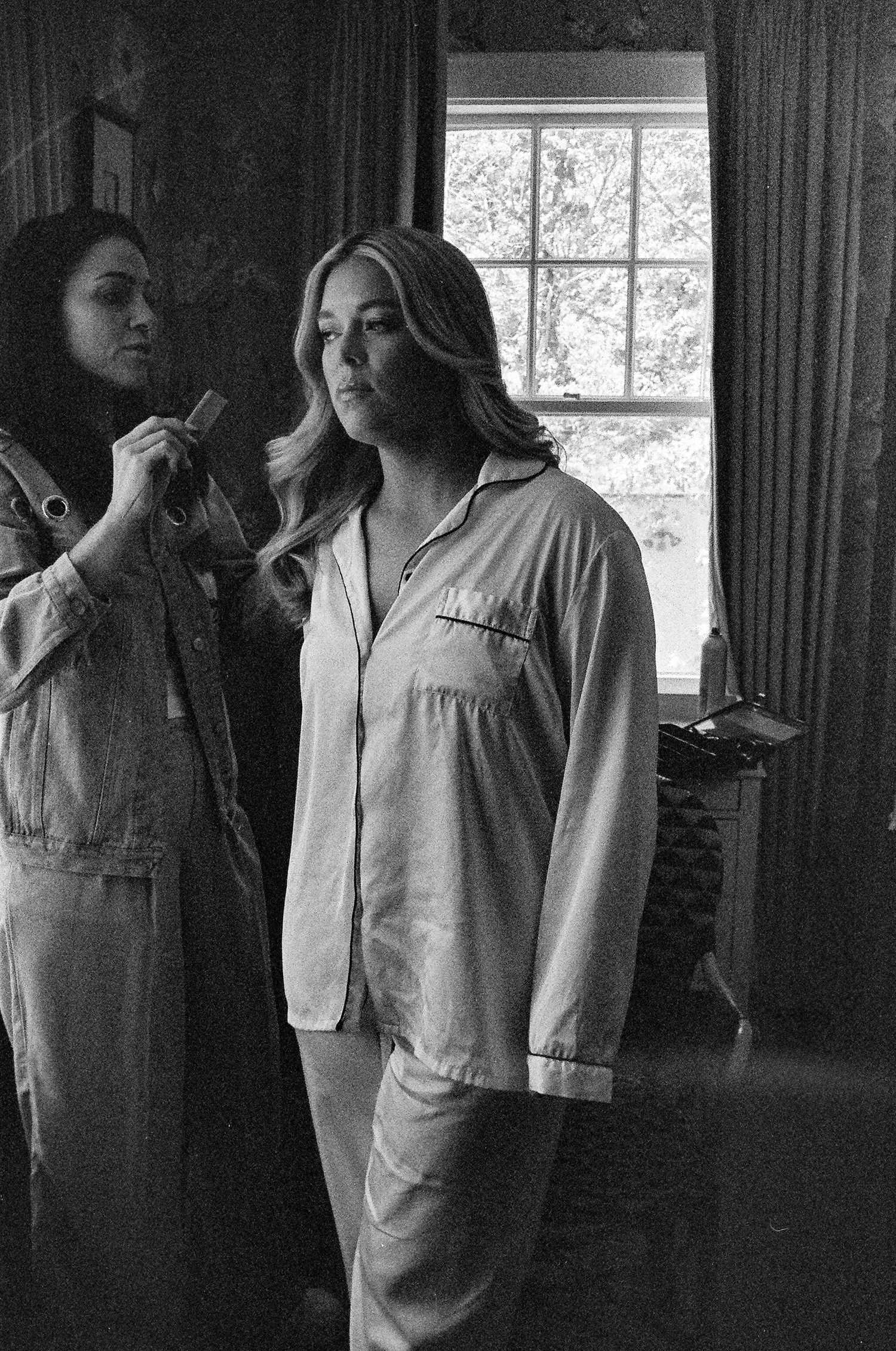 Black and white image showing two people in sleepwear by a window.